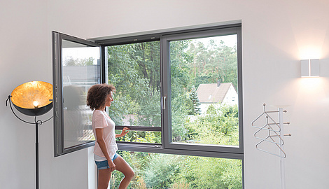 Eine Frau zieht ein Fliegengitter-Plissee an einem Fenster runter