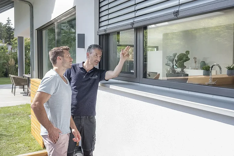Lämmermann-Monteur zeigt einem Hausbesitzer das montierte Fliegengitter am Fenster